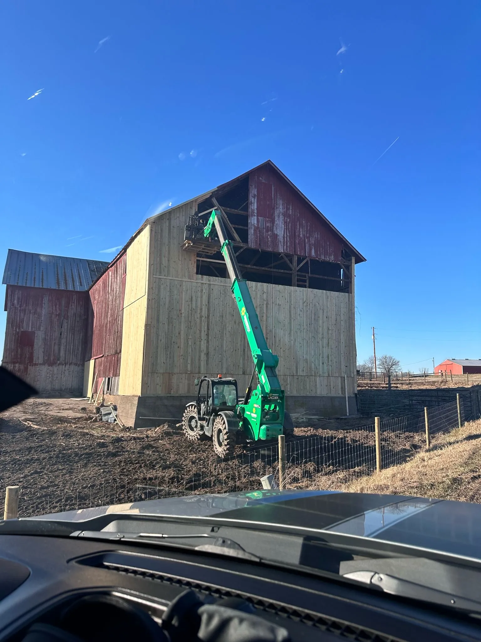 Historic red barn being restored with a boom lift on site