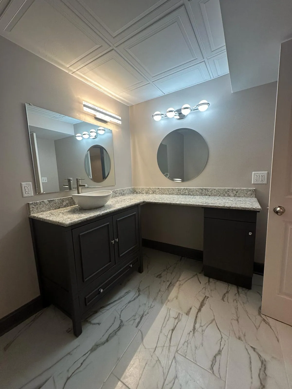 Remodeled bathroom with double vanity, round mirrors and marble-look tile floor